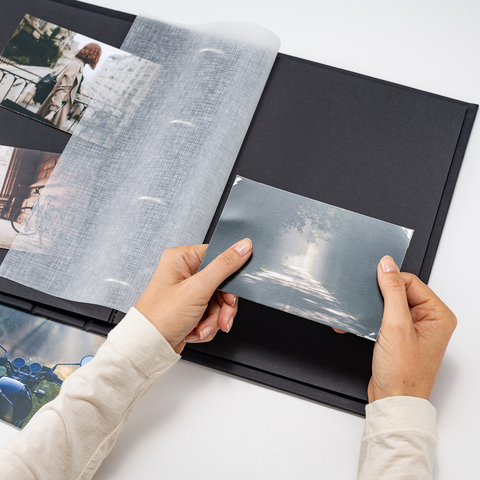 Eine Person hält ein Foto und blättert durch ein Fotoalbum mit mehreren Bildern auf schwarzen Seiten.