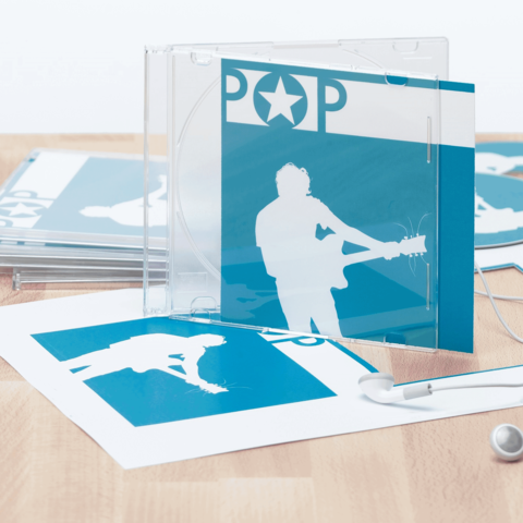 CD-Hülle mit blauem Cover und silberner Silhouette eines Musikers, umgeben von weiteren Drucksachen und Kopfhörern.