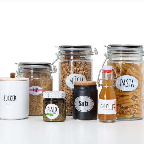 Glas med olika livsmedel: socker, ris, müsli, salt, pesto, sirap och pasta, alla märkta.