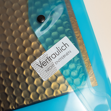 Transparente Hülle mit einem schwarzen, strukturierten Innenmaterial und einem Aufkleber, der "Vertraulich" und "Entfernen" anzeigt.