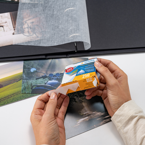 Eine Person hält eine Packung Fotopapier in der Hand, während sie Fotos in einem Album betrachtet.