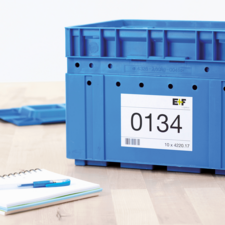 Blaue Kunststoffbox mit der Aufschrift „0134“ und einem Etikett, daneben ein Notizblock und ein Stift auf einem Tisch.