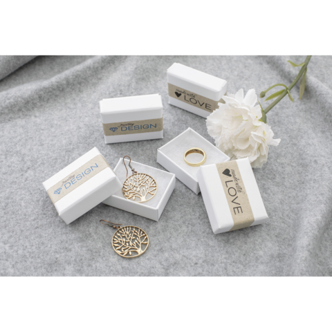 Schmuckstücke in weißen Geschenkboxen, darunter ein Baumohrring, ein Ring und eine Blume auf einem grauen Untergrund.