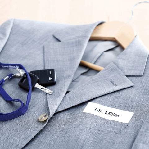 Grau Anzug mit einem Namensschild "Mr. Miller", einem Schlüsselbund und einem Schlüsselanhänger auf einem Kleiderbügel.