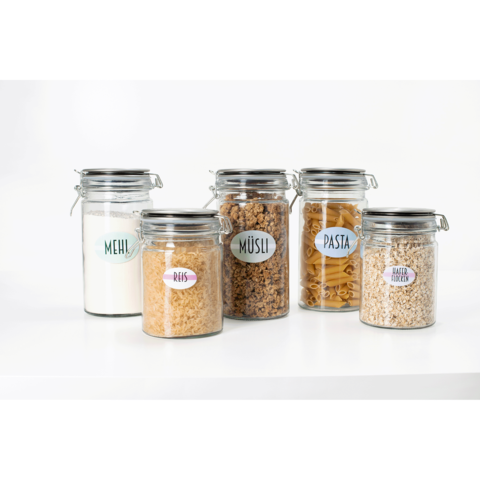 Fünf Glasbehälter mit verschiedenen Lebensmitteln: Mehl, Reis, Müsli, Pasta und Haferflocken, jeweils mit beschrifteten Etiketten.