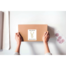 Hände halten ein braunes Paket mit einem Etikett, das "Frohe Weihnachten und ein glückliches neues Jahr" zeigt.