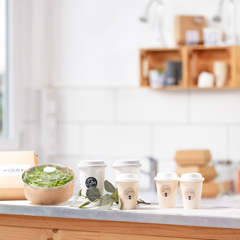 Ett träbord med en skål sallad, flera kaffekoppar och ett paket, omgiven av ett ljust, modernt kök.