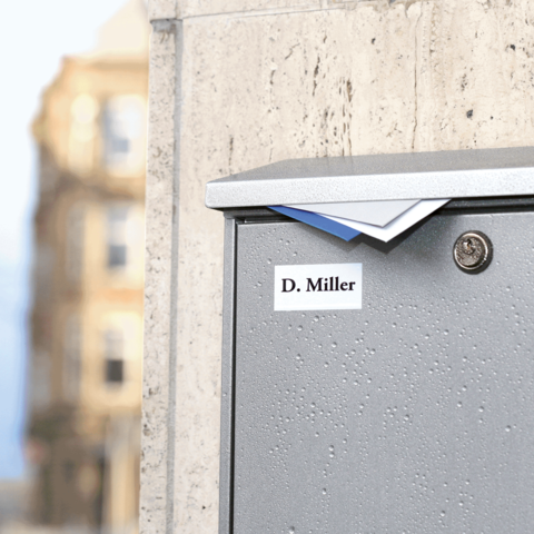 Briefkasten mit dem Namen "D. Miller" auf einer Wand, leicht geöffnet mit Briefen, die herausragen.