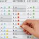 Ein Hand, die einen roten Punkt auf einem Kalenderblatt für September und Oktober anbringt, mit hervorgehobenen Daten.