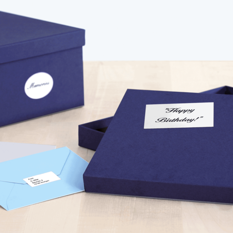 Eine geöffnete, dunkelblaue Geschenkbox mit der Aufschrift "Happy Birthday!" und einem blauen Umschlag daneben. Eine zweite Box steht im Hintergrund.