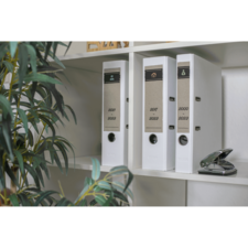 Drei weiße Ordner auf einem Regal, beschriftet mit den Jahren 2020, 2021 und 2022. Ein Heftgerät steht daneben, umgeben von einer Pflanze.