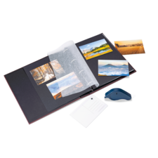 Ein Fotoalbum mit mehreren Bildern, einer transparenten Schutzfolie und einem blauen Stift liegt auf einem Tisch.