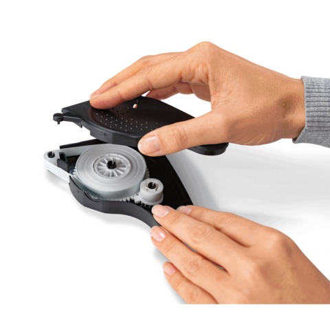 Eine Hand hält einen Korrekturroller, während die andere Hand den Mechanismus bedient. Der Korrekturroller ist geöffnet, um die Rolle sichtbar zu machen.