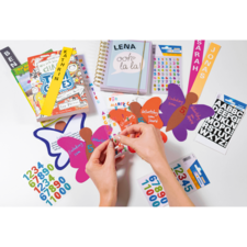 Hände, die bunte Aufkleber auf Schmetterlingsformen anbringen, umgeben von Notizbüchern und weiteren Bastelmaterialien.